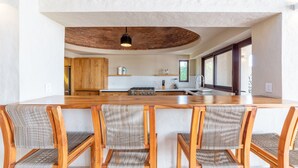 A modern kitchen with a central island, wooden chairs, and a hanging light fixture. - Casa Riviera complex with 3 pools (Bucerías)