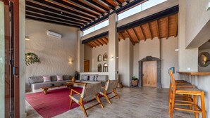 An open-plan living area with a wooden ceiling, a red rug, a sofa, a dining table, and chairs. - Casa Riviera complex with 3 pools (Bucerías)
