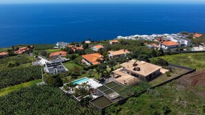 Vue aérienne d’un quartier résidentiel situé sur la côte, avec des maisons, une piscine et une vue sur l’océan.