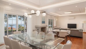 Un salon moderne avec une table à manger en verre, des chaises blanches, un canapé gris et un téléviseur à écran plat.