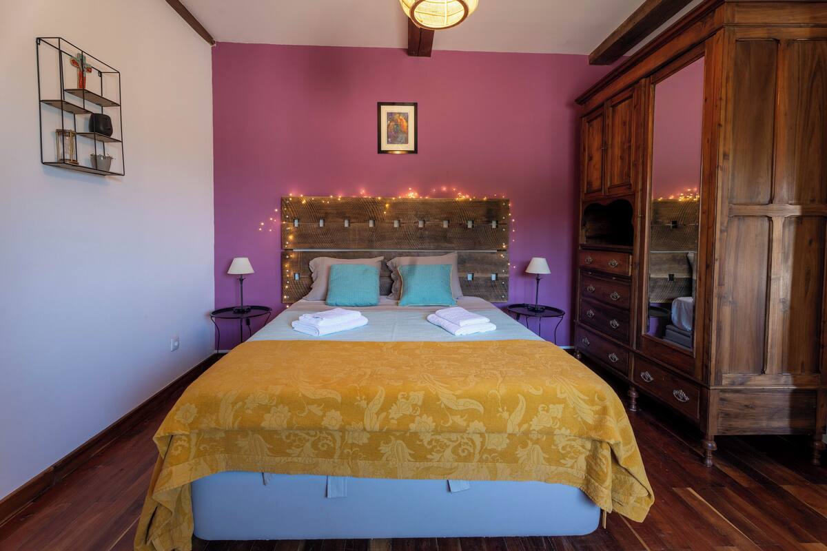 A bedroom with a bed, bedside tables, a wooden wardrobe, and a wall-mounted shelf.