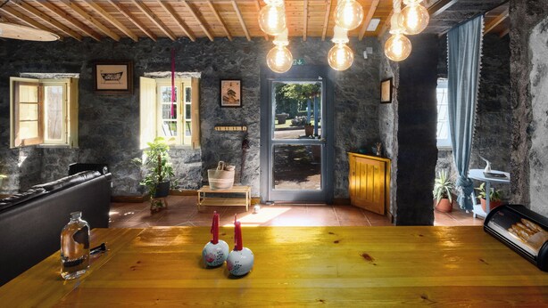 A rustic interior with exposed stone walls, wooden ceiling beams, and a wooden table with candles. - Quinta Morazes - Casa de Campo (Ribeira Grande)