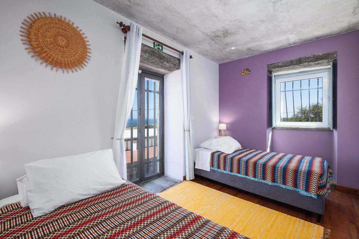 A room with two beds, a patterned rug, a window with bars, and a door leading outside.