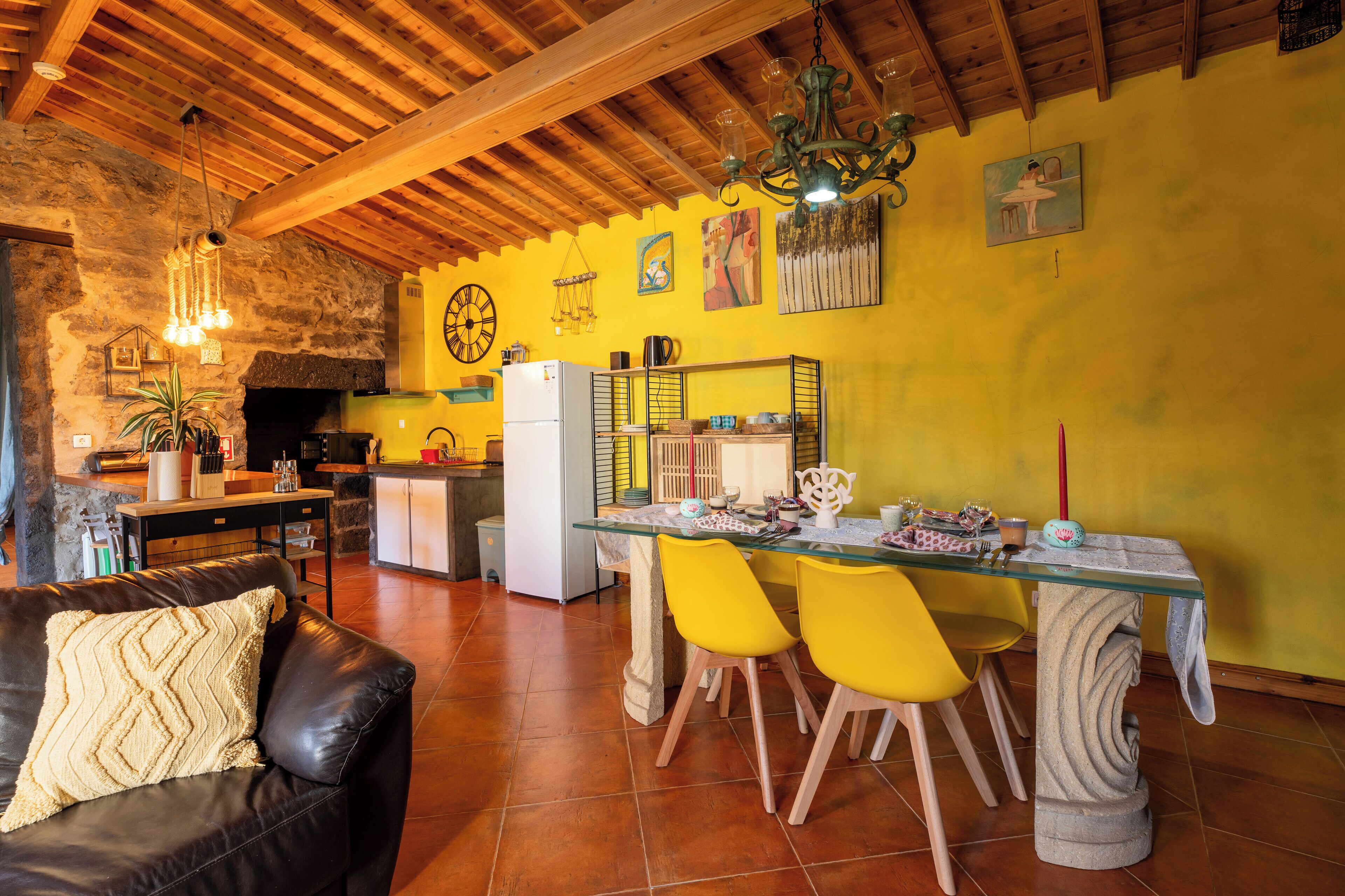 Un salon chaleureux avec un canapé en cuir, une table à manger entourée de chaises jaunes et, au fond, une cuisine.