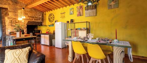 Un salon chaleureux avec un canapé en cuir, une table à manger entourée de chaises jaunes et, au fond, une cuisine.