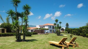 A sunny outdoor area with a pool, lounge chairs, and a building with a red roof. - Quinta Morazes - Casa de Campo (Ribeira Grande)
