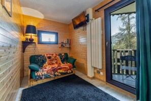 A cozy cabin room with a wooden interior, a sofa with a colorful blanket, a small table with a lamp, and a view of the outdoors through a glass door. - 50m from ski slopes, 5th floor, view forest, balcony, tv, 28m², Les Orres (Les Orres)