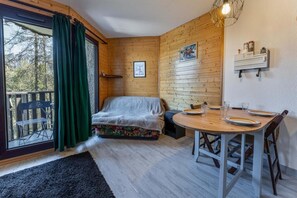 Ein gemütliches Zimmer mit einem Bett, einem Esstisch für zwei Personen und einem Fenster mit Blick auf Bäume.
