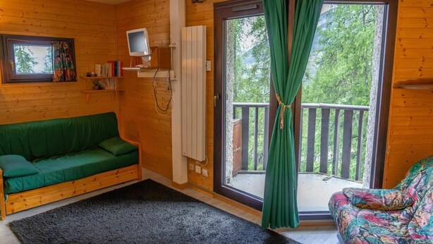 Ein gemütliches Zimmer mit einem grünen Sofa, einem Fernseher und einem großen Fenster mit Vorhängen.