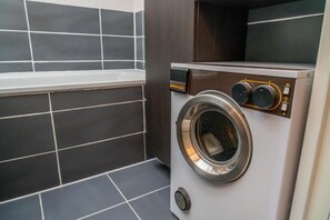 A compact, modern laundry room with a built-in washer and dryer, dark tiled walls, and a small window. - 50m from ski slopes, 5th floor, view forest, balcony, tv, 28m², Les Orres (Les Orres)