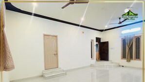 Una habitación amplia con piso de baldosas, una puerta de madera, una escalera y un ventilador de techo.