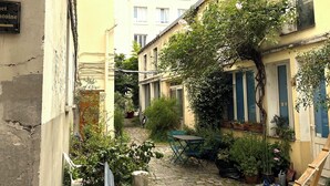 A narrow cobblestone alley with a bench, potted plants, and a building with a yellow facade. - Fbg St-antoine, le Marché Aligre (Paris)