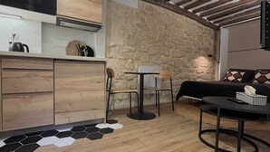 A modern kitchen with wooden cabinets, a stone wall, and a dining area with a round table and chairs. - Fbg St-antoine, le Marché Aligre (Paris)