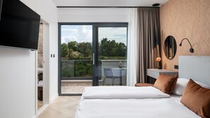 A modern hotel room with a large bed, a TV, a desk with a chair, and a balcony with a table and chairs. - Luxury Villa David's two heated pools 38m2 bbq Seaview (Podstrana)