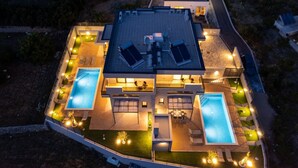 A modern house with two swimming pools, a covered patio, and a well-lit outdoor area. - Luxury Villa David's two heated pools 38m2 bbq Seaview (Podstrana)