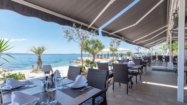 An outdoor dining area with tables set for two, overlooking a beach and the sea. - Luxury Villa David's two heated pools 38m2 bbq Seaview (Podstrana)