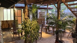 An outdoor patio area with wooden furniture, including chairs and a table, surrounded by various potted plants. - Ceylon Beach Haven Uppuveli (Trincomalee)