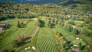 An aerial view of a golf course with multiple fairways, sand bunkers, and a backdrop of forested hills. - 4BR/4Bath Townhome w/AC, Walk to Ski, Golf, Tennis, Hiking and More! (Sugar Mountain)