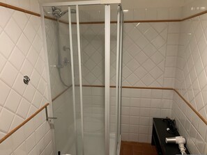 Ένα ντους με γυάλινη πόρτα, λευκά πλακάκια στους τοίχους και ξύλινο πλαίσιο.