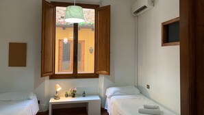 A small, clean room with two beds, a desk with a lamp, and a window with wooden shutters. - Sdrucciolo dei Pitti First Floor (Florence)