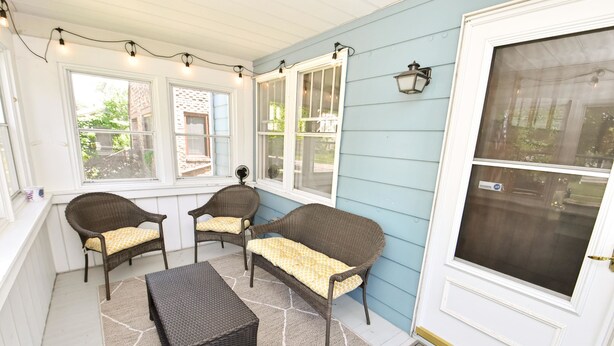 A covered porch with wicker furniture, a patterned rug, and a view of the outside. - Updated Bungalow Steps to Notre Dame 410 (South Bend)