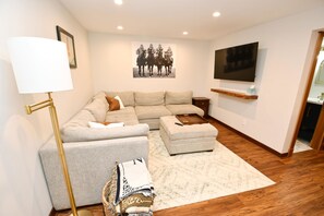 A modern living room with a sectional sofa, a floor lamp, a mounted TV, and a framed picture on the wall. - Updated Bungalow Steps to Notre Dame 410 (South Bend)