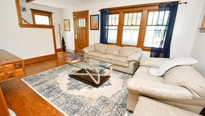 A living room with a beige sofa, a glass coffee table, and a patterned rug. - Updated Bungalow Steps to Notre Dame 410 (South Bend)