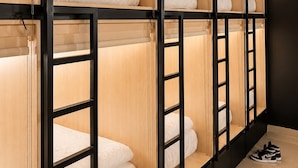 A row of bunk beds with wooden frames and white bedding, each with a towel hanging above. - WeStay Capsule Hostel (Dubai)