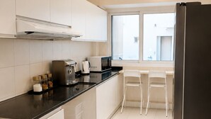 A modern kitchen with white cabinets, a black countertop, a refrigerator, and a window providing natural light. - WeStay Capsule Hostel (Dubai)