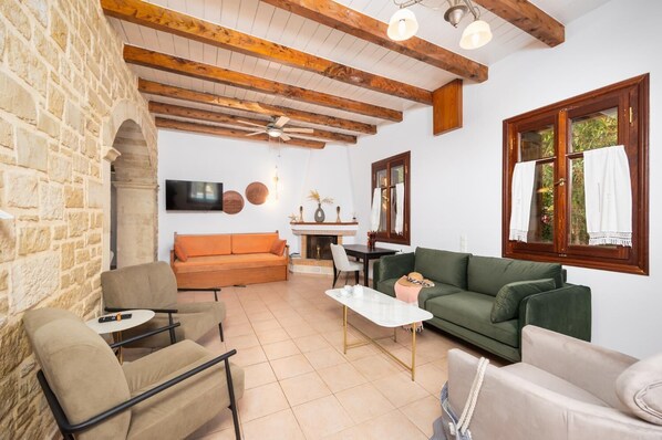 A cozy living room with stone walls, wooden beams, a green sofa, a beige armchair, and a white coffee table. - Villa Lotus - Three Bedroom Villa, Sleeps 6 (Prines)