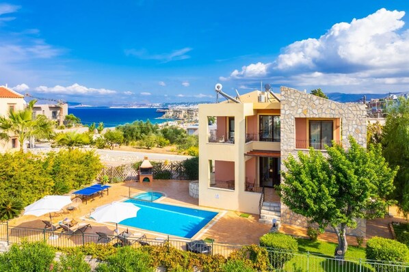 A two-story building with a swimming pool, outdoor seating, and a view of the sea.