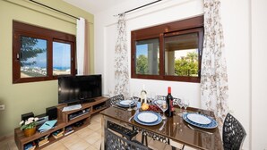Un comedor con una mesa dispuesta para dos, un televisor y una estantería con libros y un jarrón de flores.