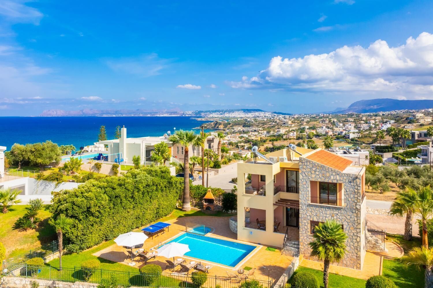 A modern villa with a swimming pool, surrounded by lush greenery and a view of the sea.