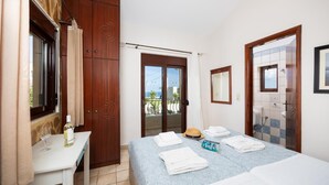 Quarto de hotel com cama, mesa com garrafa e copo, armário, banheiro com espelho e vista para o exterior.