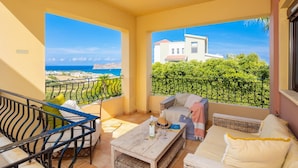 Varanda com vista para o mar e edifícios, mobiliada com sofá, cadeiras e mesa.