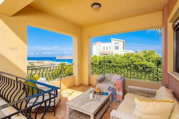 Un balcon avec vue sur la mer et les bâtiments, aménagé avec un canapé, des fauteuils et une table.