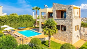Uma casa moderna de dois andares com piscina, fachada de pedra e vista para a paisagem ao redor.