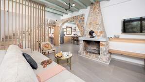 Un salon moderne avec une cheminée en pierre, un canapé, un coin repas et une cuisine visible à travers une arche ouverte.