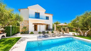 Une maison à deux étages avec une piscine, un espace salon extérieur et un mur en pierre.