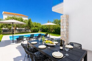 Ein Essbereich am Pool mit einem Tisch für zwei Personen, Gartenstühlen und Sonnenschirmen.