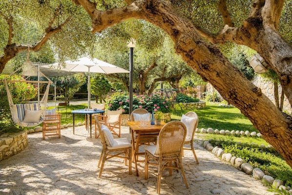 An outdoor patio with wicker furniture, a hanging chair, and a table with a vase.
