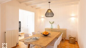 Een eetgedeelte met een houten tafel, witte stoelen, een schaal fruit en een hangende lamp.