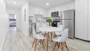 Eine moderne Küche mit weißen Schränken, einem Edelstahl-Kühlschrank, einer Mikrowelle und einem Essbereich mit einem weißen Tisch und Stühlen.