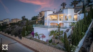 Ein mehrstöckiges Haus mit Balkon, umgeben von viel Grün und einer Steinmauer.