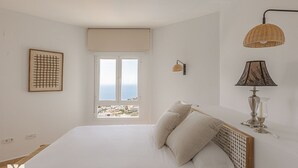 Ein Schlafzimmer mit einem großen Bett, einem Fenster mit Blick, einer Wandlampe und einem gerahmten Bild.