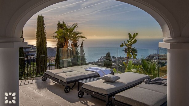 Ein Balkon mit zwei Liegestühlen, einer Glasreling und Blick auf das Meer und die Stadt.