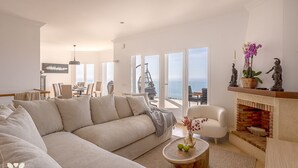 Ein geräumiges Wohnzimmer mit einem großen, beigefarbenen Ecksofa, einem runden Couchtisch aus Holz und einem Kamin mit Backsteinoptik.