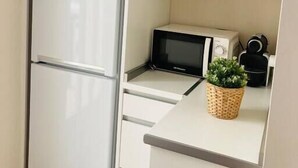 A compact kitchen with a white refrigerator, a microwave, and a toaster. There is a small potted plant on the countertop.