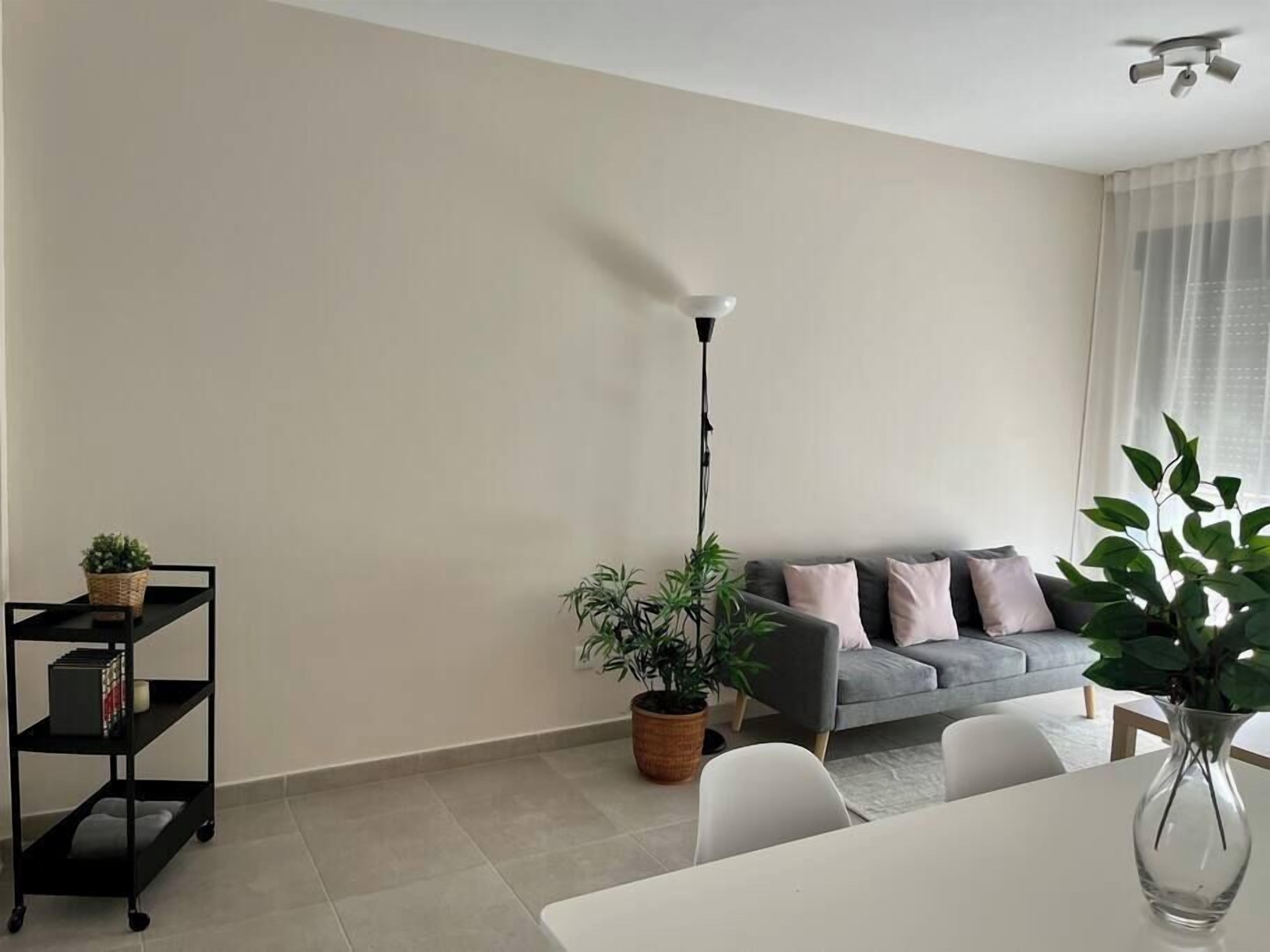 A modern living room with a grey sofa, a dining table, and a potted plant.