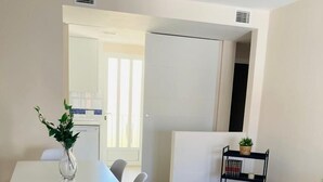 A modern dining area with a white table and chairs, a vase with green plants, and a small black shelf with items.